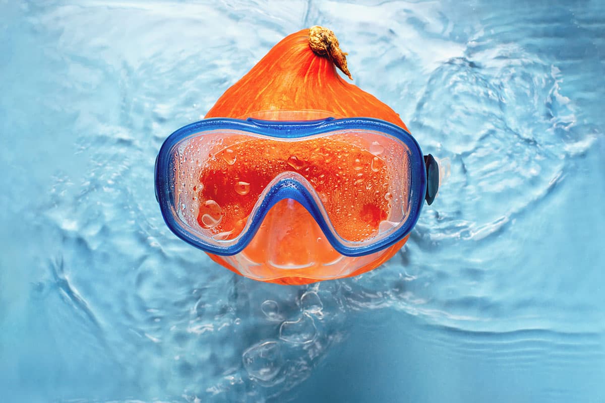 Orange pumpkin swimmer in a mask in blue water. Halloween concept Fiberglass swimming pool Halloween decorating idea